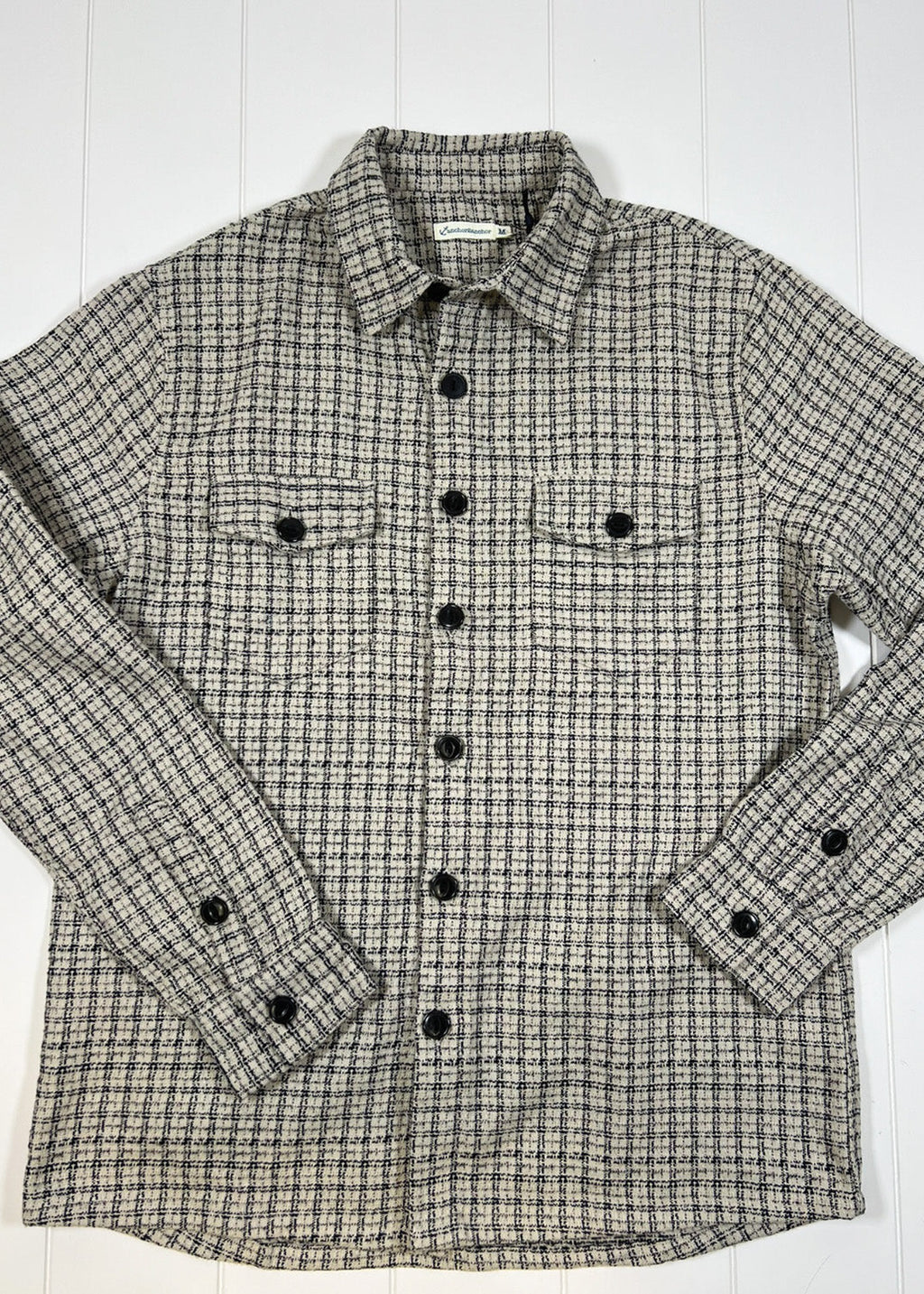Plaid shirt with black buttons on a white wooden surface