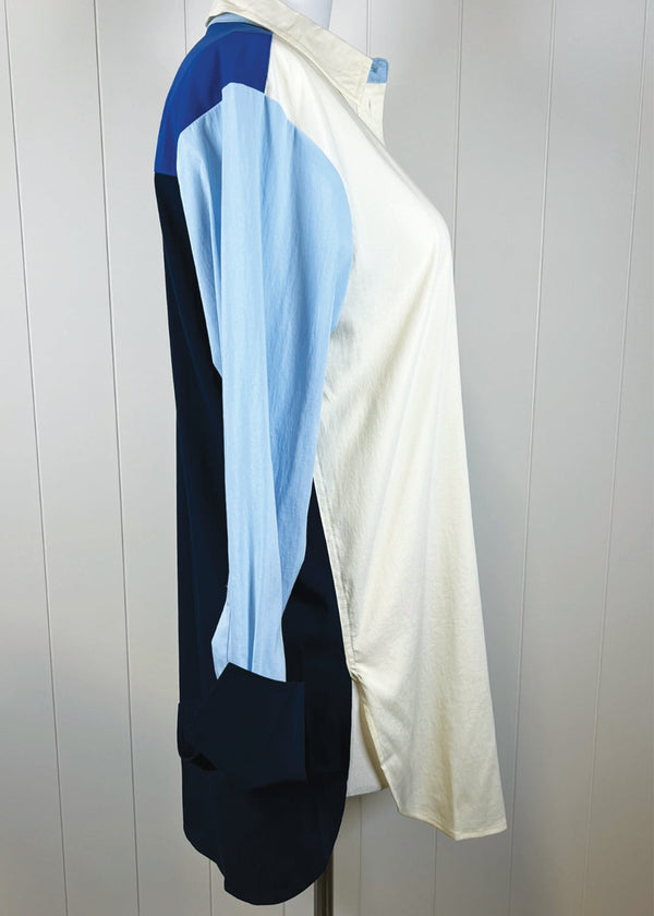 Color-blocked garment with blue, white, and black sections on a hanger against a light background