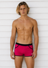 Man wearing pink swim shorts with a black waistband against a white wooden background
