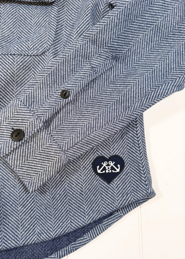 Blue herringbone patterned shirt with a logo on a white background