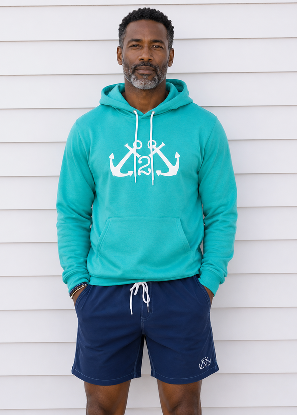 Man wearing a turquoise hoodie with anchor design and navy shorts against a white background