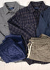 Collection of men's clothing including shirts and shorts on a white background