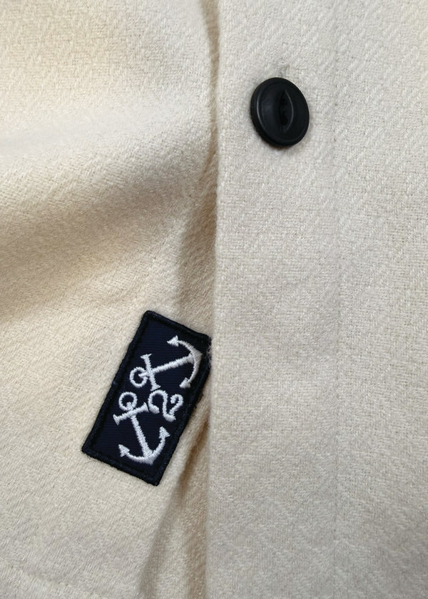 Close-up of a white coat with a black button and embroidered label featuring an anchor design.