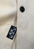 Close-up of a white coat with a black button and embroidered label featuring an anchor design.