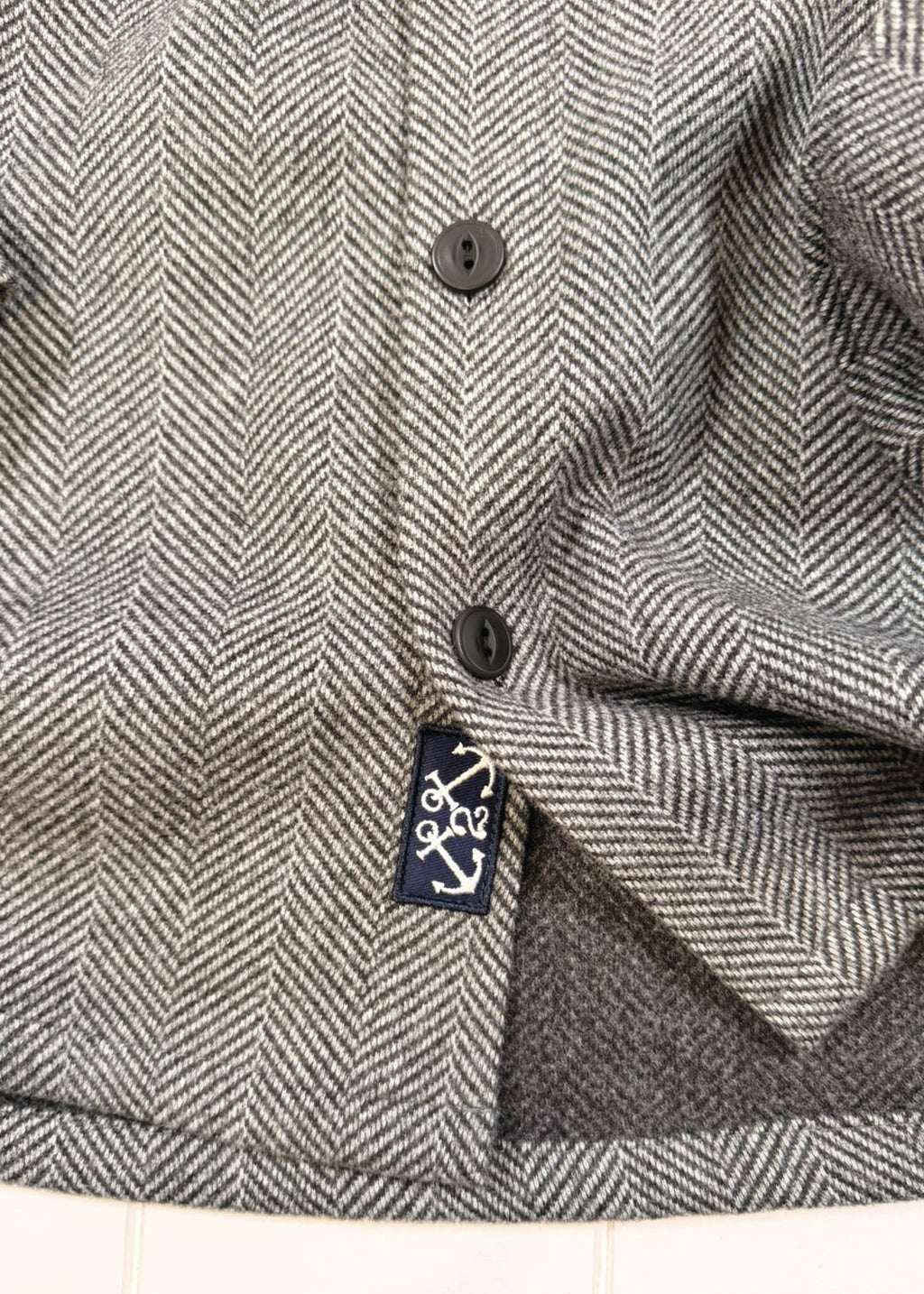 Close-up of a herringbone-patterned fabric with a brand label on a white background