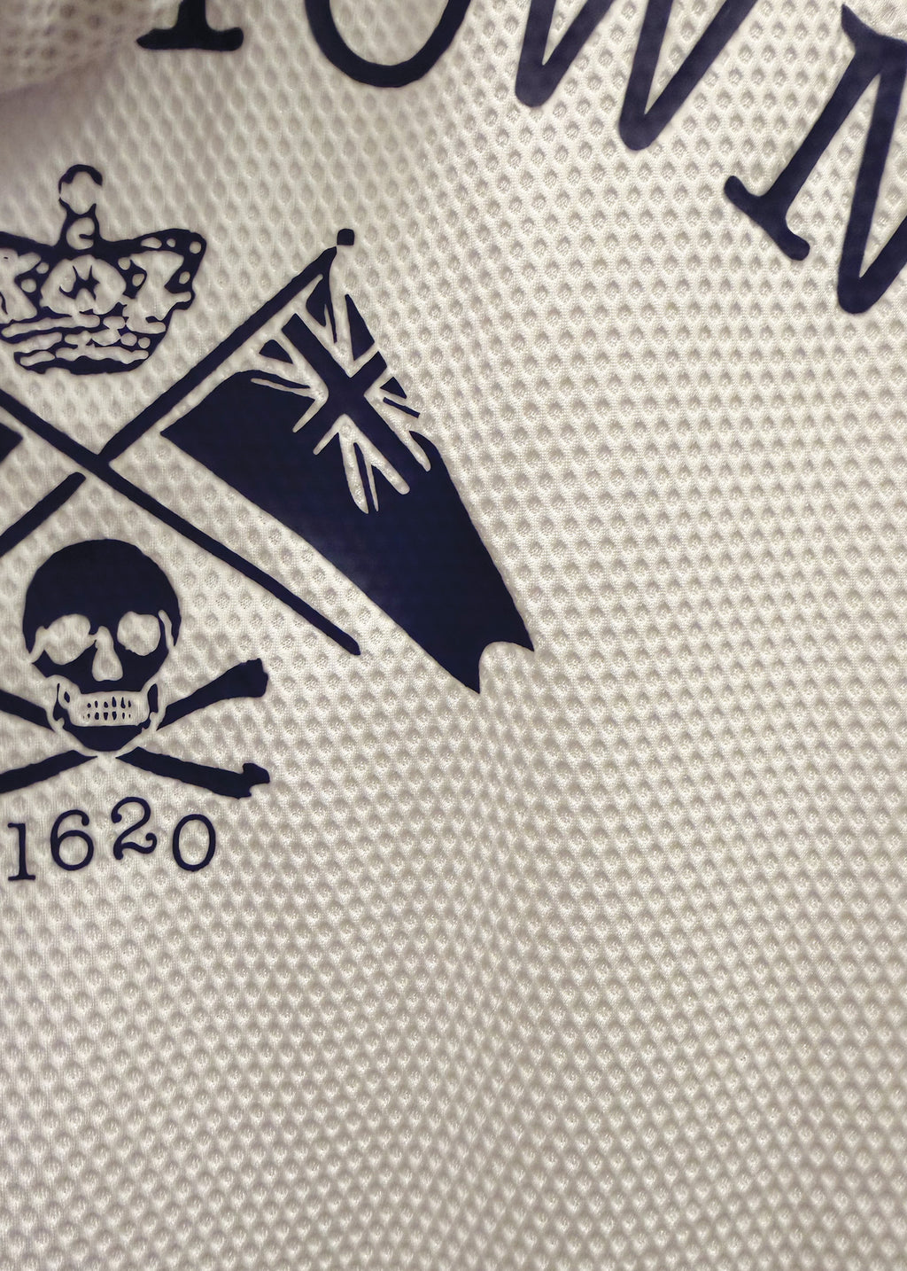 Close-up of a white textured fabric with a navy blue printed graphic featuring a crown, flag, skull and crossbones, and the number 1620.