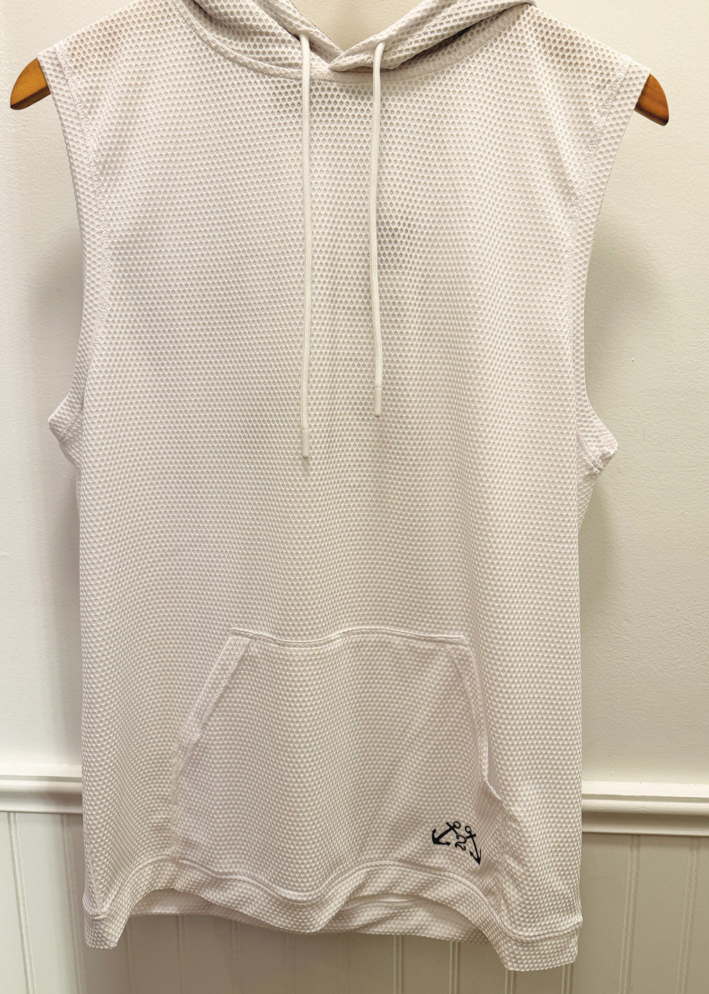 A sleeveless white mesh hooded top with drawstrings and a front kangaroo pocket, hanging on wooden hangers against a white paneled wall.