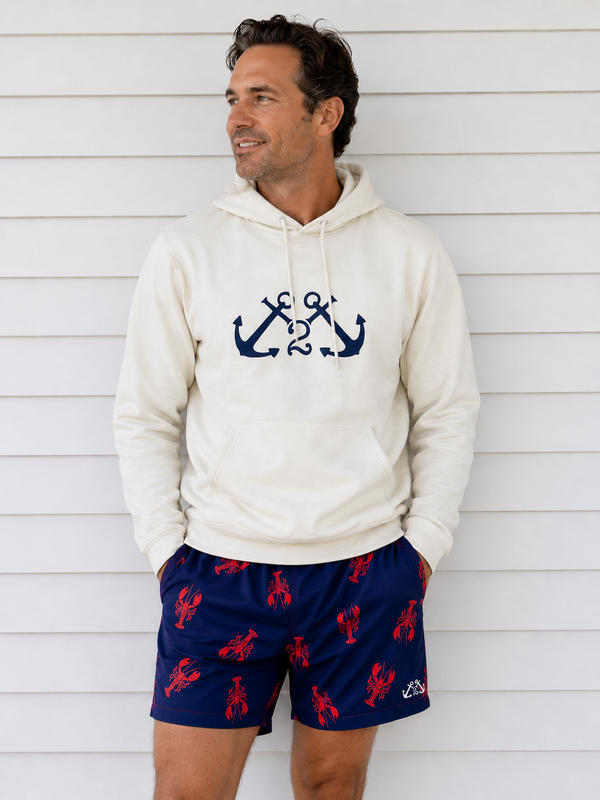 Man wearing a cream hoodie with anchor design and navy shorts with red lobster pattern against a white wooden background