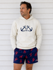Man wearing a cream hoodie with anchor design and navy shorts with red lobster pattern against a white wooden background