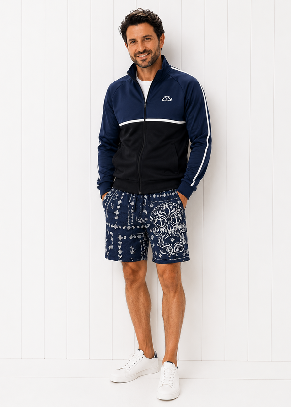 Man wearing a navy tracksuit with white stripes and patterned shorts against a white background