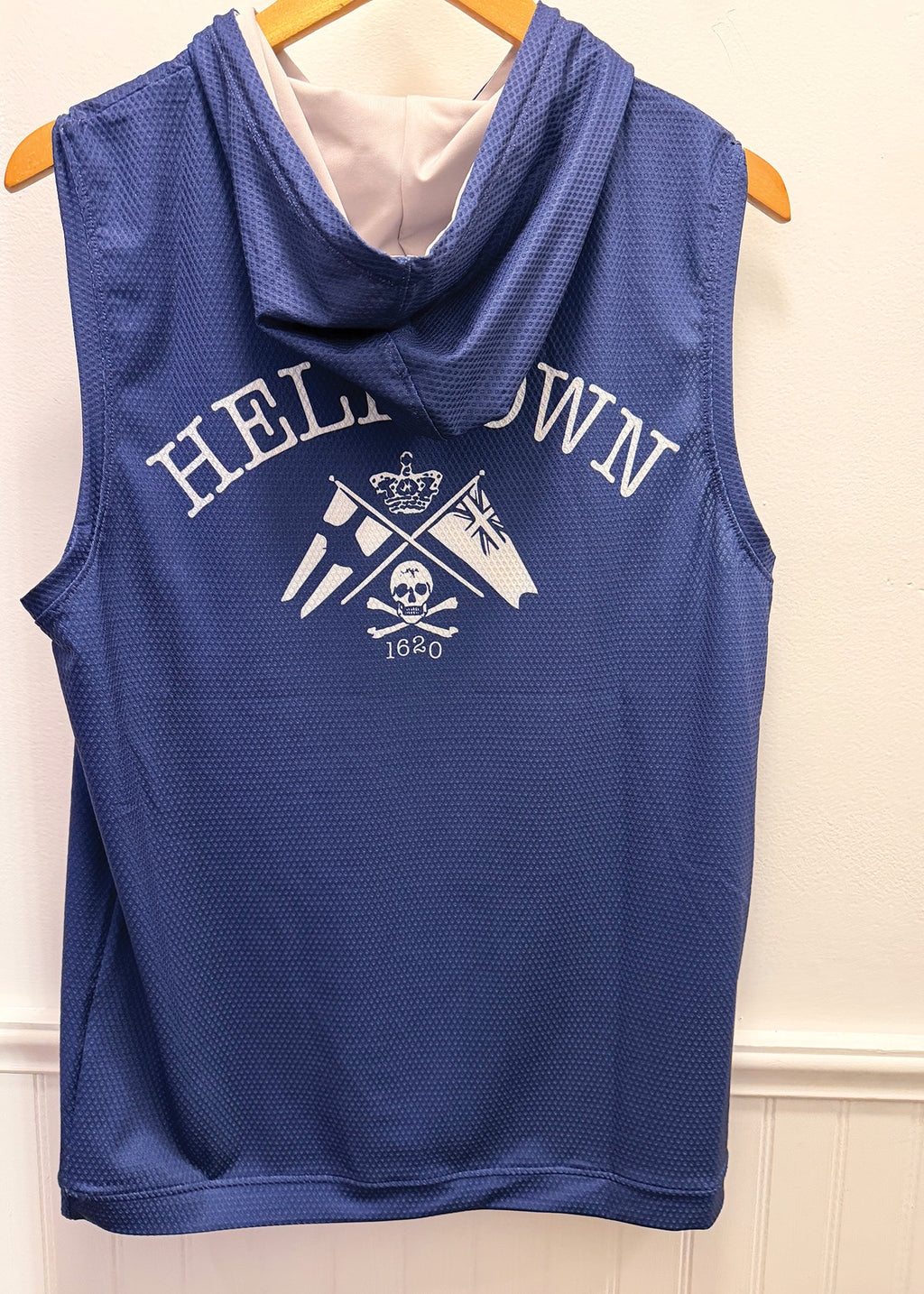 A blue sleeveless mesh hooded top hanging on a wooden hanger against a white paneled wall. The front has a white graphic reading 'HELL OWN' above crossed flags, a crown, and '1660' with a skull motif.