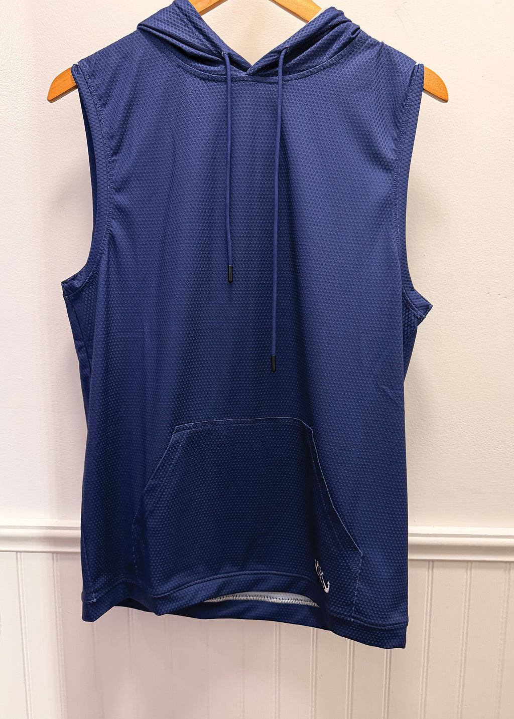 A sleeveless navy blue hooded athletic vest with a drawstring hood and front kangaroo pocket, hanging on a wooden hanger against a white paneled wall.
