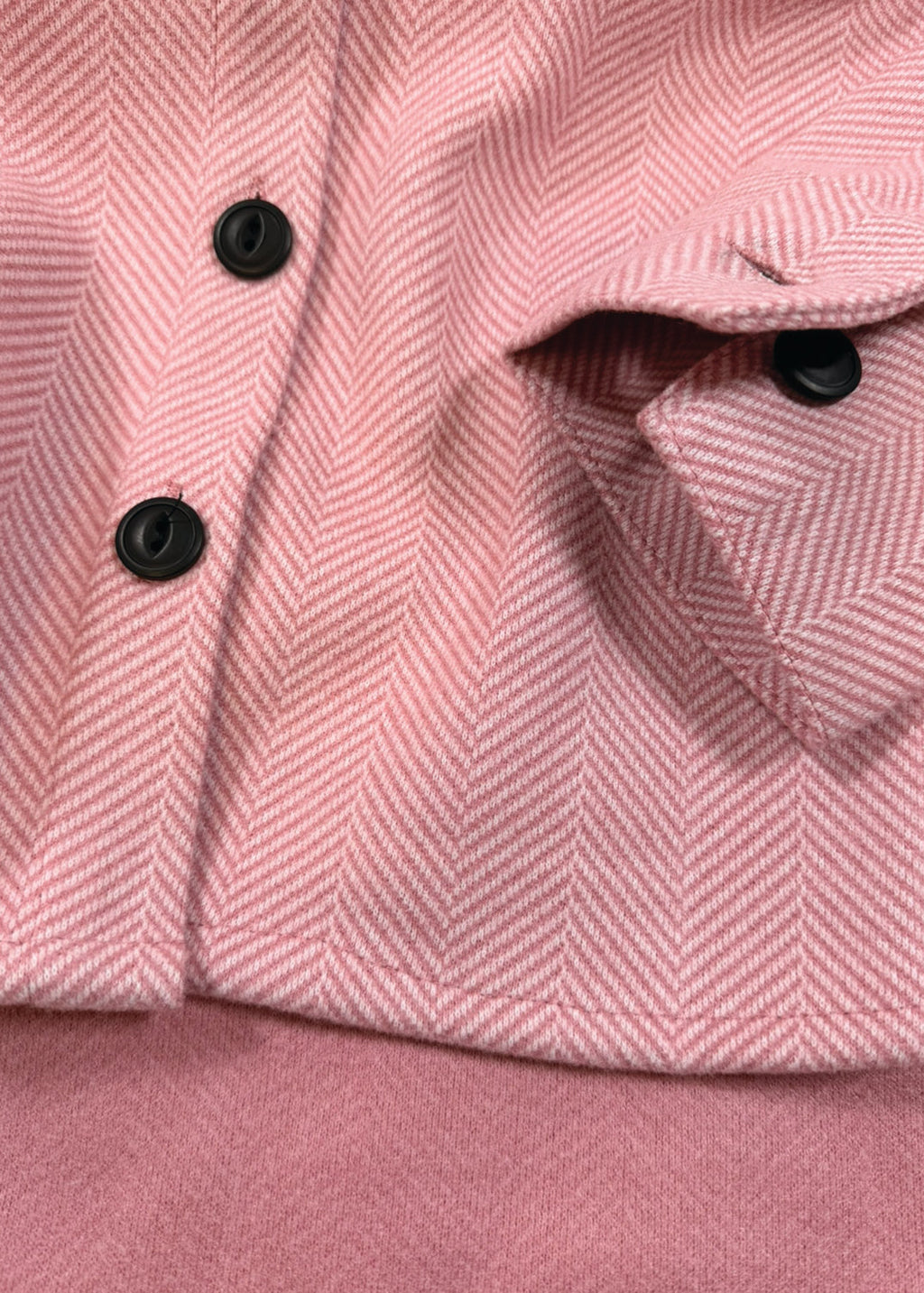 Close-up of a pink herringbone patterned fabric with black buttons.