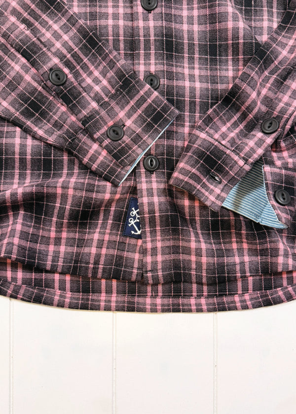 Close-up of a pink and black plaid shirt with a brand logo on a white background