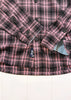Close-up of a pink and black plaid shirt with a brand logo on a white background
