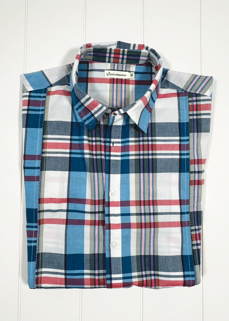 Folded plaid shirt with visible brand label on a white wooden background