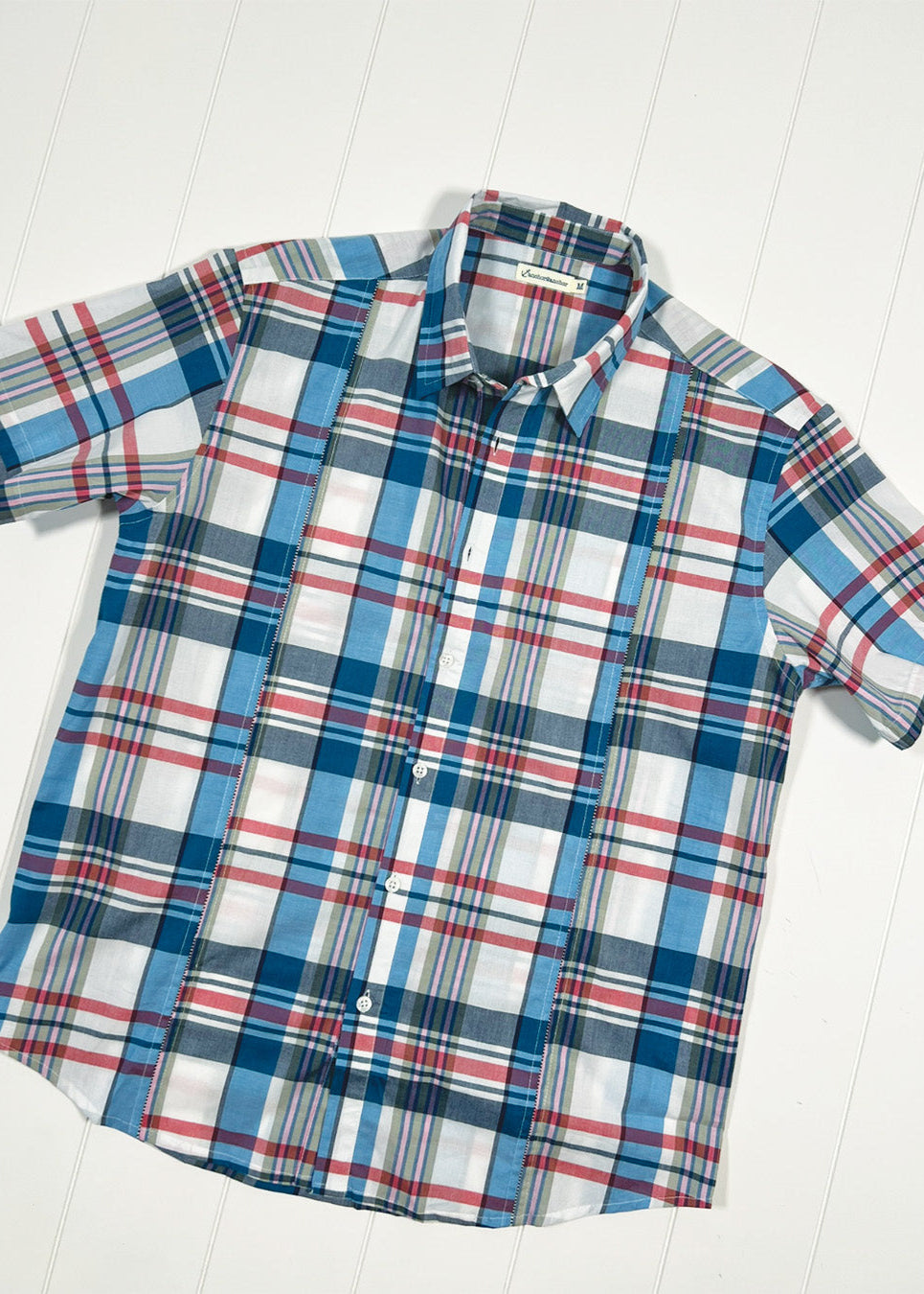 Plaid short-sleeve shirt with blue, red, and white pattern on a light wooden surface