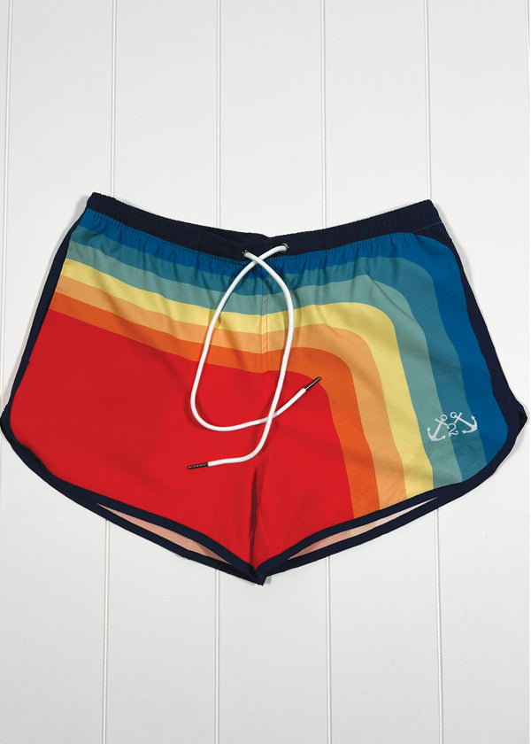 Colorful swim shorts with a rainbow pattern on a white wooden background