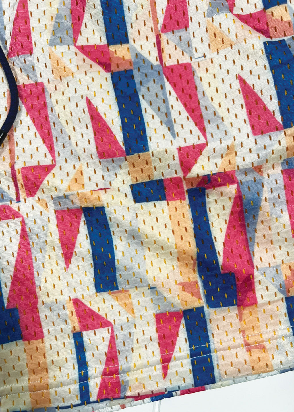 Colorful geometric patterned fabric with pink, blue, and yellow triangles on a white background.