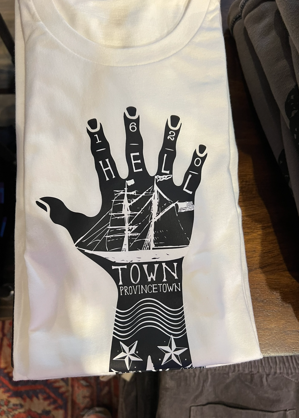 White t-shirt with black hand graphic and text on a wooden surface