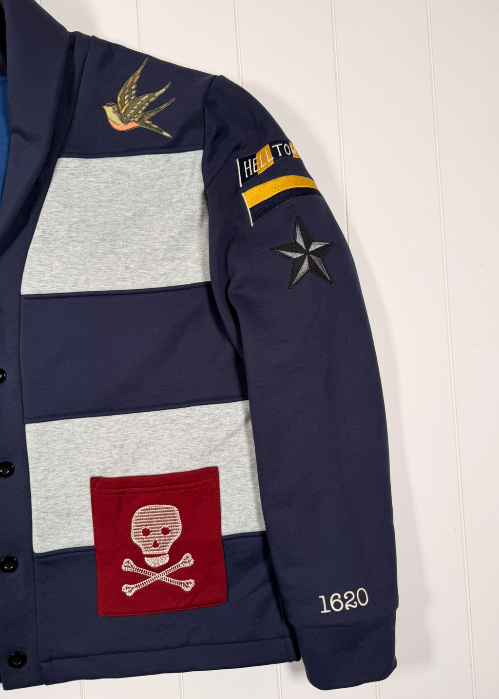 Navy blue jacket with various patches including a skull and crossbones design, displayed against a white background.
