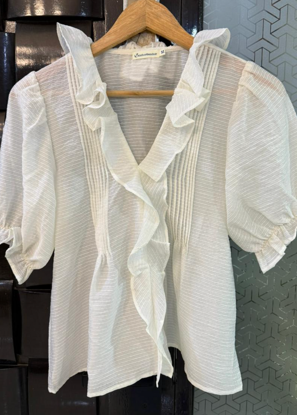White blouse with ruffled sleeves on a hanger against a dark background