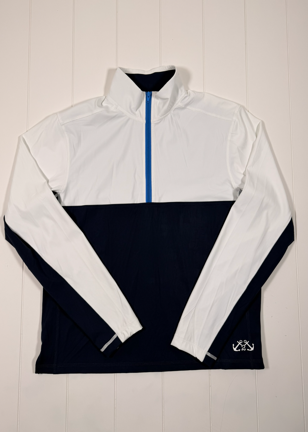 White and navy half-zip pullover with a brand logo on a wooden background