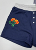 Navy blue shorts with floral embroidery and brand logo on a light gray background