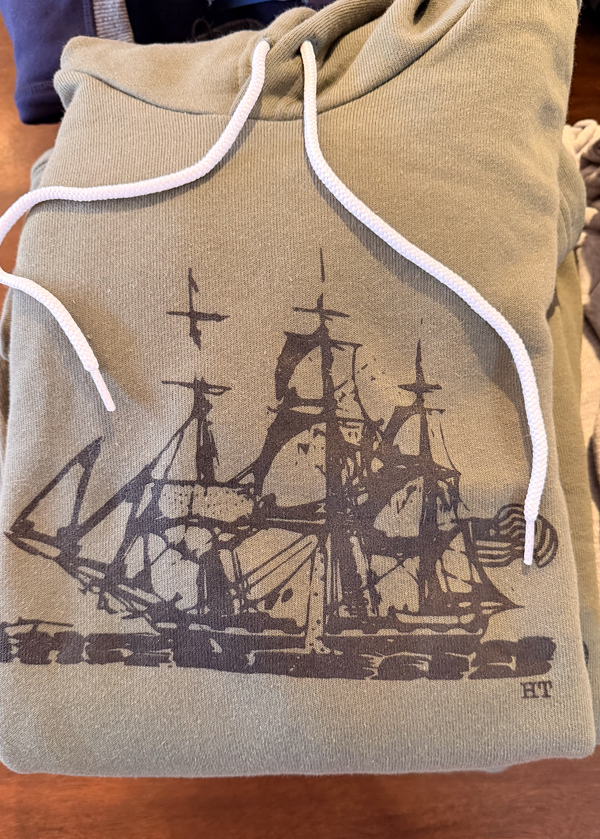 Folded hoodie with a ship design and 'HT' logo on a wooden surface
