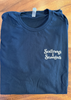 A folded navy blue t-shirt with 'Scallywags & Scoundrels' printed in white gothic-style lettering on the left chest, laid flat on a wooden surface.
