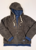 A dark brown sherpa fleece zip-up hoodie jacket with a navy blue lining, cream-colored drawstrings, and navy blue ribbed cuffs and hem, laid flat on a white wood panel background.