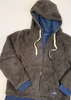 A dark gray sherpa fleece zip-up hoodie jacket with a blue lining, cream-colored drawstrings, and blue ribbed cuffs and hem, laid flat on a white wooden background.