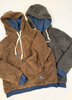 Two teddy fleece zip-up hoodies laid flat on a white wood background, one in brown and one in dark gray, both with blue lining and white drawstrings.