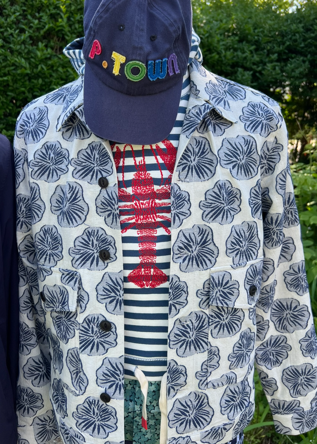 Person wearing a patterned jacket over a striped shirt with a navy cap.