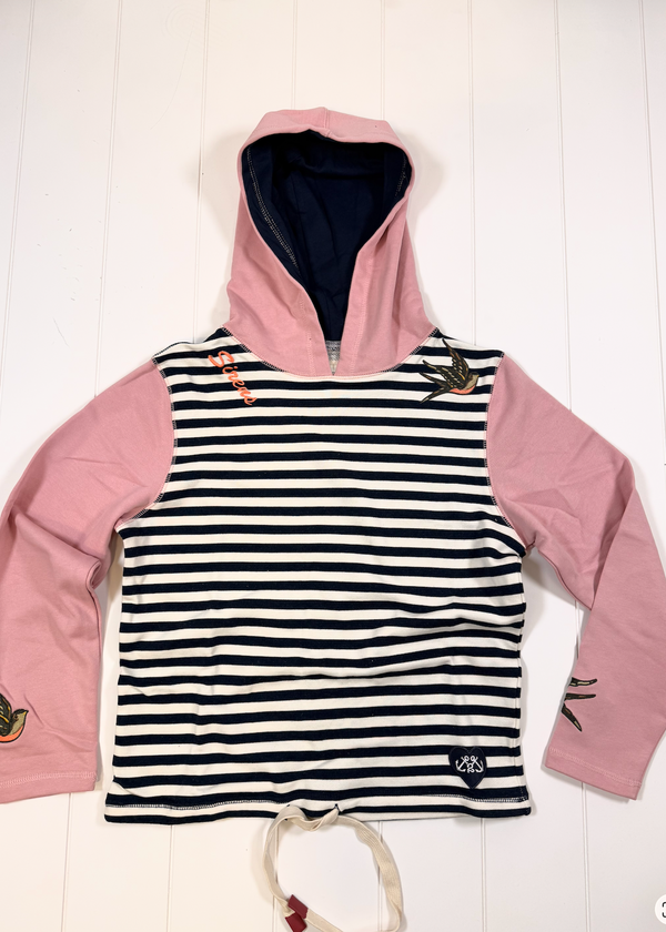 A children's hooded long-sleeve top laid flat on a white wood background. The front has horizontal black and white stripes, while the hood, inner lining, and sleeves are light pink.