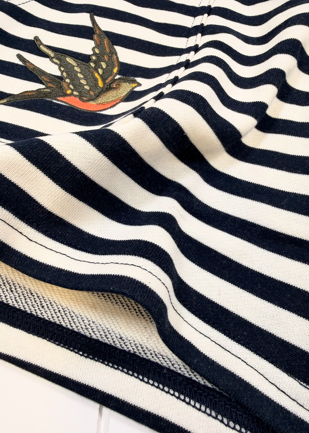 Close-up of a navy and cream striped knit garment with a small embroidered swallow motif near the upper left area.