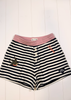 Black and white striped shorts with a dusty pink elastic waistband, featuring a button fly closure, a swallow patch on the left leg, and a small black logo patch on the right leg.