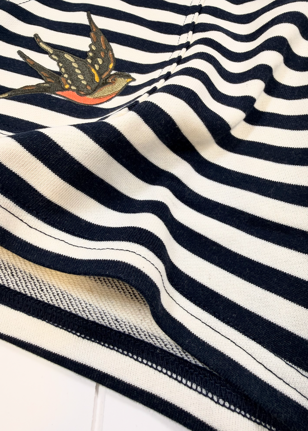 Close-up of a navy and off-white striped knit fabric with a small embroidered swallow motif near the upper left area.