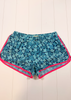 Blue patterned athletic shorts with a butterfly print and bright pink trim, laid flat on a white wood plank background.