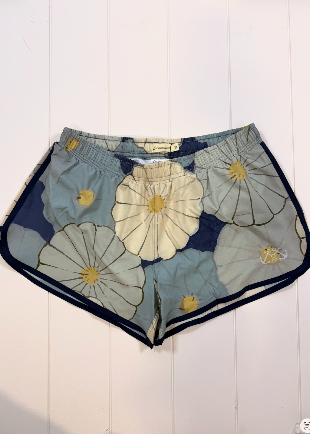 A pair of women's shorts featuring a large-scale floral print with navy blue, light blue, and cream flowers outlined in black, finished with a contrasting navy blue hem.