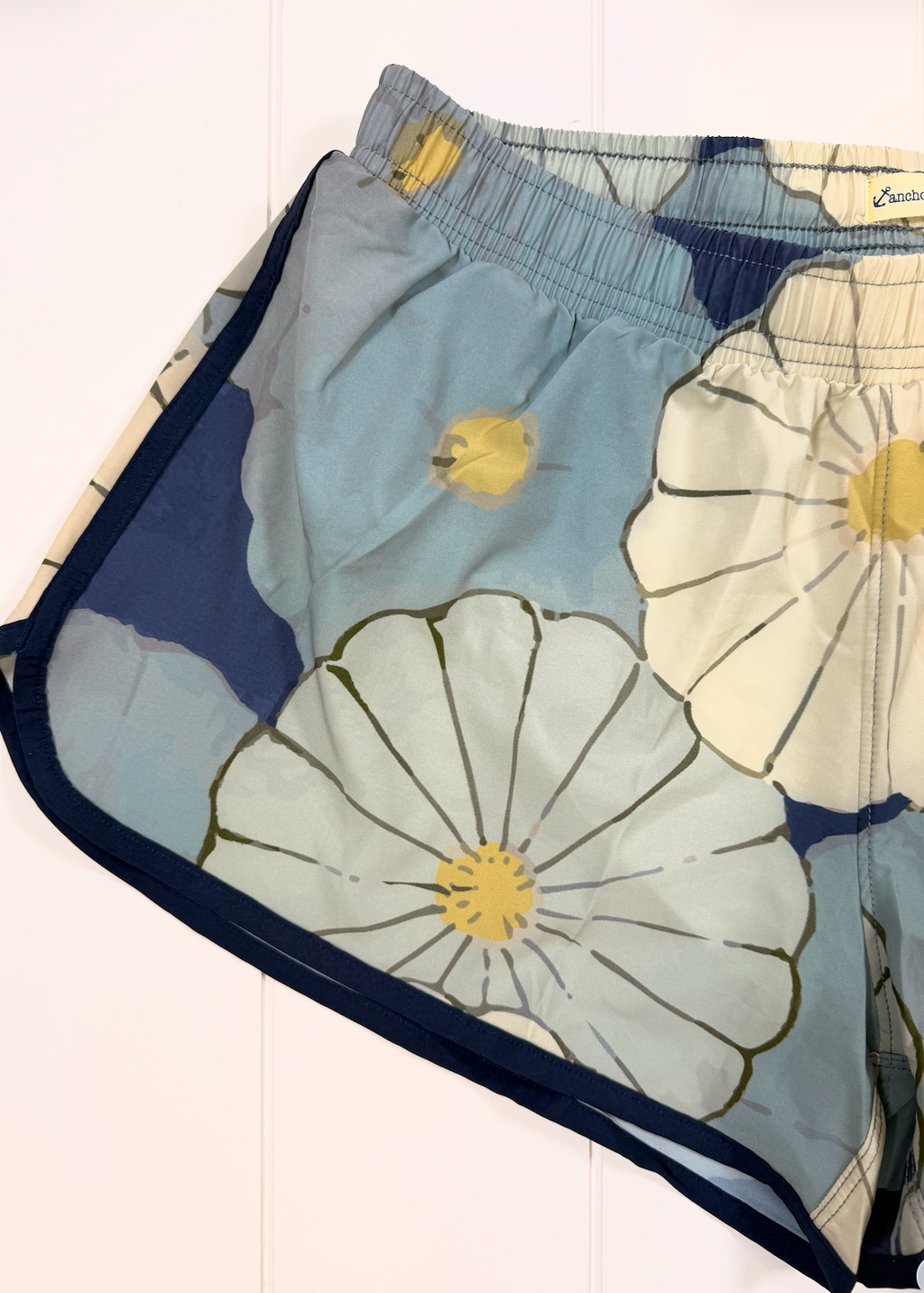 A close-up of a pair of sheer mesh shorts featuring a floral print with large light blue, cream, and navy flower motifs, accented with yellow centers and dark navy trim.