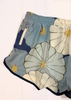 Light blue and navy floral print shorts with a white zipper pocket, laid flat against a white paneled background.