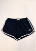 Navy blue athletic shorts with white side stripes and a white embroidered anchor logo on the left leg, laid flat on a white wood plank background.