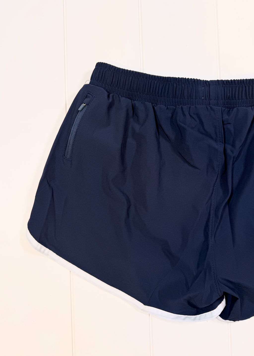 Navy blue athletic shorts with an elastic waistband and a side zippered pocket, shown against a white paneled background.