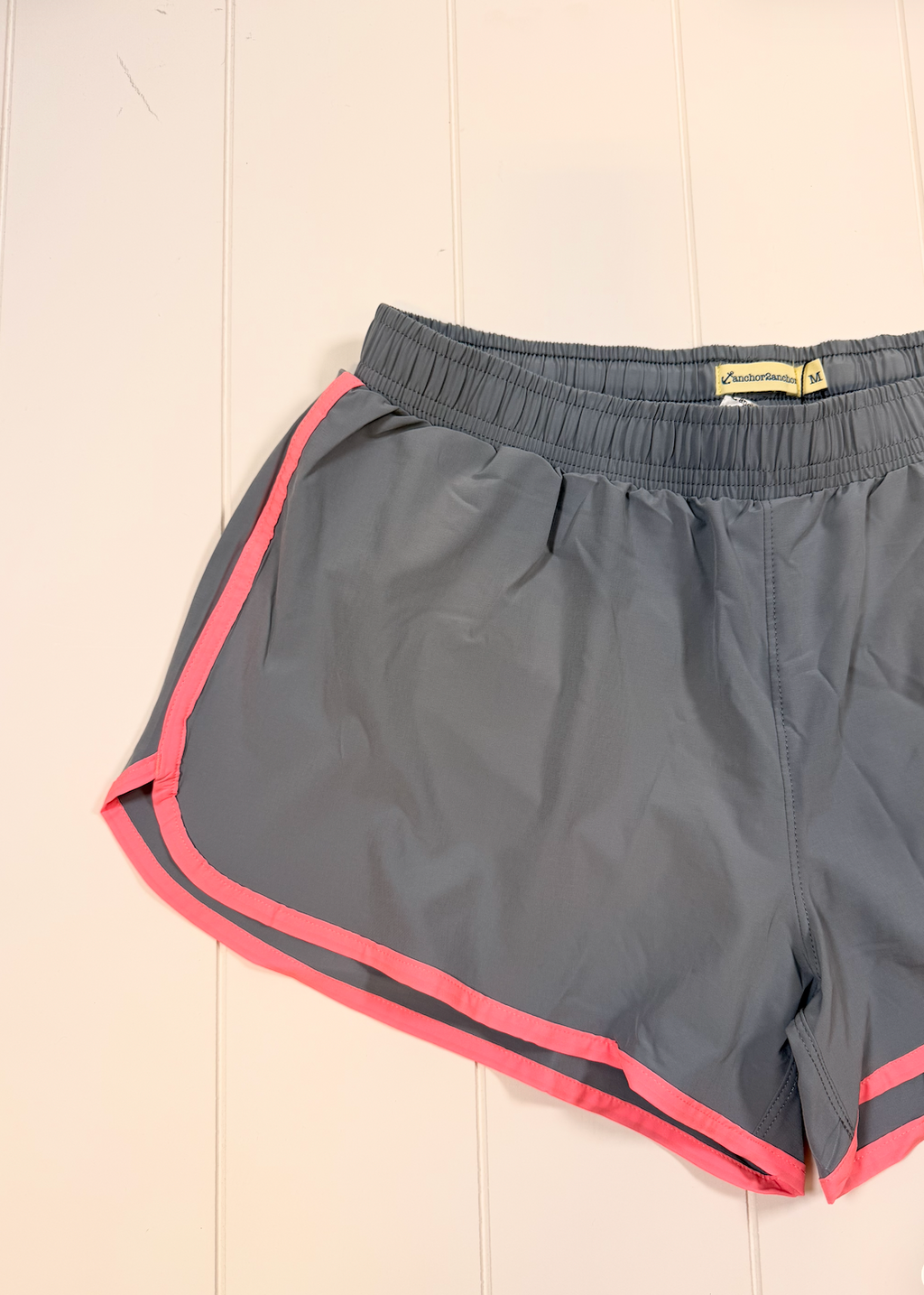 Gray athletic shorts with pink piping trim along the side seams and hem, laid flat on a white paneled background.