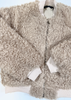 A beige curly sherpa fleece zip-up jacket with ribbed cream cuffs and collar, laid flat on a white background.