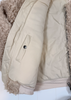 Close-up of a quilted beige jacket with a cream sherpa lining and a fluffy beige fleece collar, showing a side pocket with a snap button.
