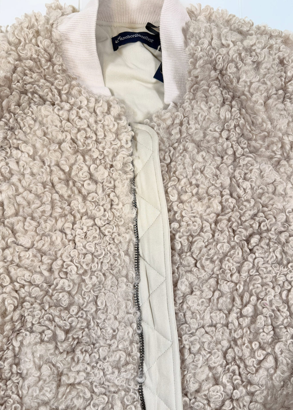Close-up of a cream-colored sherpa fleece jacket with a quilted front zipper and ribbed collar.