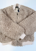 A beige sherpa fleece zip-up jacket with ribbed cream cuffs and hem, laid flat on a white wooden background.
