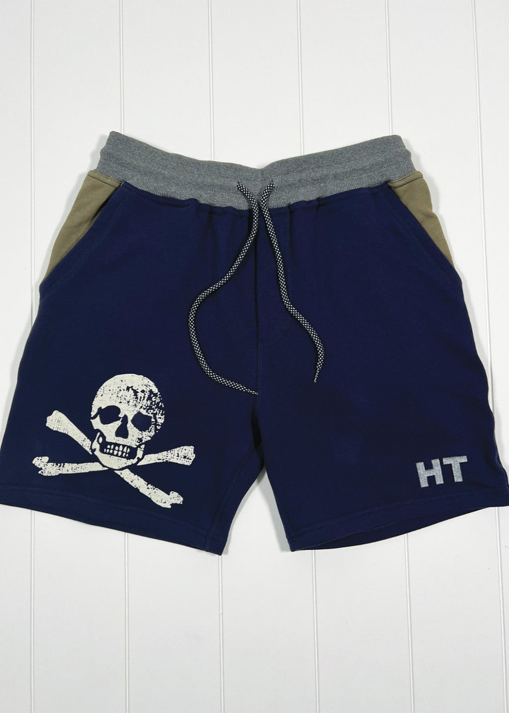 Navy shorts with skull and crossbones design and 'HT' branding on a white wooden background